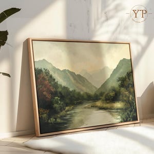 May include: A framed landscape painting depicting a river winding through a valley with lush green trees and mountains in the background. The sky is a soft, muted blue with hints of pink and orange.