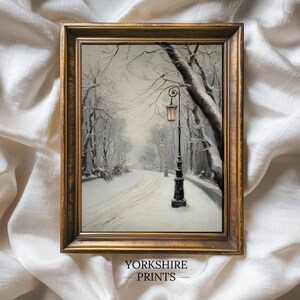 Peut inclure: Une impression encadrée d'une scène hivernale enneigée avec un chemin sinueux et des lampadaires. L'œuvre est dans un cadre doré et porte le texte "YORKSHIRE PRINTS". La palette de couleurs est principalement en niveaux de gris avec des touches de lumière chaude.