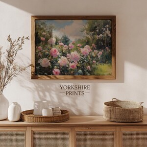 Puede incluir: Una pintura enmarcada de un jard&iacute;n con rosas rosadas en flor. La pintura est&aacute; colgada en una pared sobre un armario de madera con una cesta de mimbre y jarrones blancos.