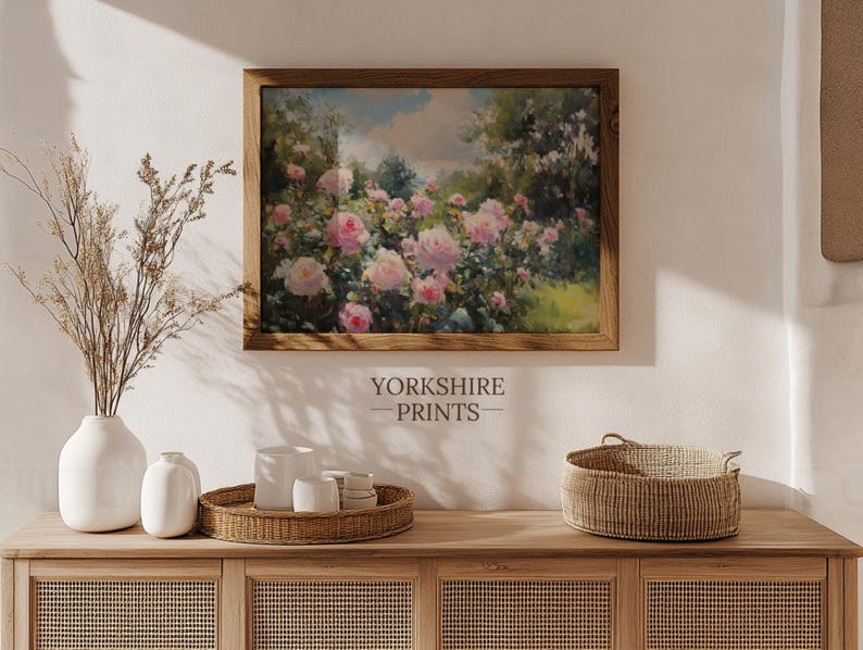 Puede incluir: Una pintura enmarcada de un jard&iacute;n con rosas rosadas en flor. La pintura est&aacute; colgada en una pared sobre un armario de madera con una cesta de mimbre y jarrones blancos.