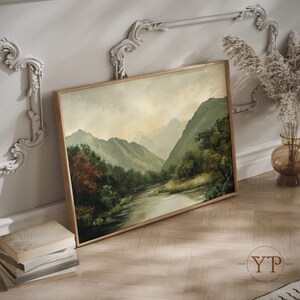 May include: A framed painting of a misty mountain landscape with a river winding through the valley. The painting is in a light wood frame and is hanging on a white wall.