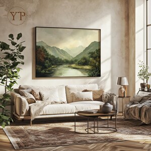 May include: A beige sofa with white throw pillows sits in a living room with a large framed landscape painting of a river and mountains. A small round coffee table with a book and a vase sits in front of the sofa. A rug with a brown and beige pattern covers the floor.