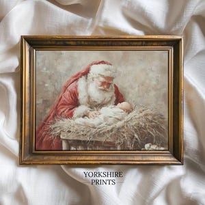 May include: A framed print featuring Santa Claus in a red suit with white trim, looking down at a baby in a manger. The artwork has a vintage style with a gold-colored frame. The text "YORKSHIRE PRINTS" is visible at the bottom.