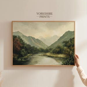 May include: A framed painting of a landscape with a river winding through a valley surrounded by green mountains. The sky is a soft gray with hints of pink and orange.