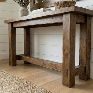 May include: A rustic, solid wood console table with a natural finish. The table features a rectangular top and thick, square legs. The wood grain is visible, adding to the table's charm. The table is 60 inches long, 16 inches wide, and 30 inches high.