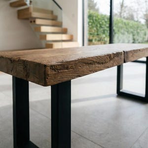 May include: A rustic wooden bench with a natural, textured surface. The bench is supported by black metal legs, creating a contrast between the wood and metal. The design is simple and modern, suitable for indoor use.