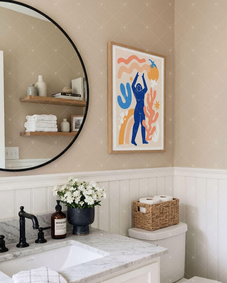 Puede incluir: Una l&aacute;mina de arte enmarcada que muestra una figura humana azul rodeada de formas abstractas en naranja, amarillo y azul claro sobre un fondo crema. La obra est&aacute; expuesta en un marco de madera clara sobre una pared beige en un ba&ntilde;o.