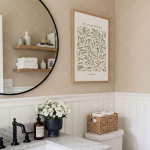 Puede incluir: Una l&aacute;mina de arte mural enmarcada con un patr&oacute;n bot&aacute;nico de hojas de William Morris y el texto William Morris y Frankfurt, expuesta en un ba&ntilde;o con lavabo de m&aacute;rmol, grifo negro, espejo redondo y estantes de madera.
