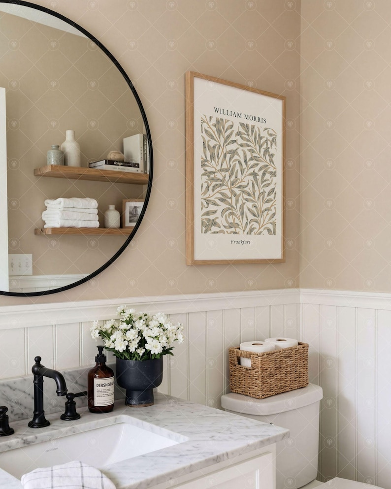 Puede incluir: Una l&aacute;mina de arte mural enmarcada con un patr&oacute;n bot&aacute;nico de hojas de William Morris y el texto William Morris y Frankfurt, expuesta en un ba&ntilde;o con lavabo de m&aacute;rmol, grifo negro, espejo redondo y estantes de madera.