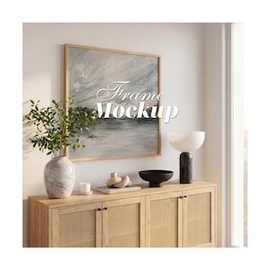 May include: A square wooden picture frame containing a landscape painting of a lake under a cloudy sky, with the text Frame Mockup overlaid in white script. The frame is displayed on a wall above a light wood cabinet with cane door panels.