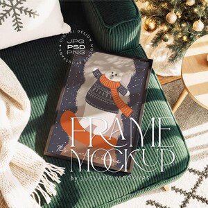 Puede incluir: Un marco negro con una ilustración de invierno que muestra un oso polar con un suéter y bufanda. La imagen está colocada sobre un sillón de pana verde. El texto "FRAME MOCKUP" es visible. Es una maqueta.