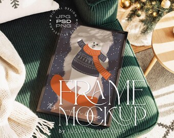 Puede incluir: Un marco negro con una ilustración de invierno que muestra un oso polar con un suéter y bufanda. La imagen está colocada sobre un sillón de pana verde. El texto "FRAME MOCKUP" es visible. Es una maqueta.