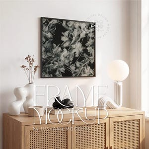Puede incluir: Una impresión artística abstracta enmarcada en negro con pinceladas blancas cuelga sobre un mueble de madera. El mueble está adornado con jarrones decorativos, una lámpara y el texto "FRAME MOCKUP by JUSVANA MOCKUPS".