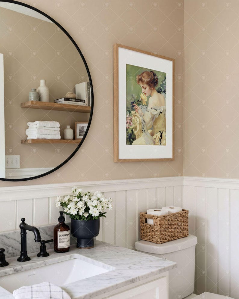 Puede incluir: Un ba&ntilde;o con un espejo redondo de marco negro que refleja estantes de madera con toallas blancas, un retrato enmarcado de una persona con una flor amarilla, un lavabo de m&aacute;rmol con grifo negro y una cesta de mimbre sobre el inodoro.