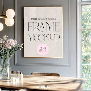 Puede incluir: Una maqueta enmarcada con el texto "FRAME MOCKUP" y "3:4 RATIO" en un círculo rosa. El marco tiene un borde dorado y está colgado en una pared gris. Una mesa con un jarrón de flores y una ventana están en primer plano.