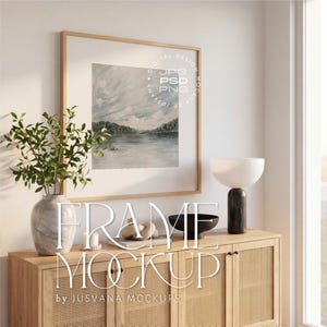 Puede incluir: Una pintura de paisaje en acuarela enmarcada cuelga sobre un mueble de madera. El mueble tiene puertas de caña tejida y está decorado con un jarrón con vegetación, un cuenco negro y una lámpara moderna. El texto de la maqueta del marco es visible.