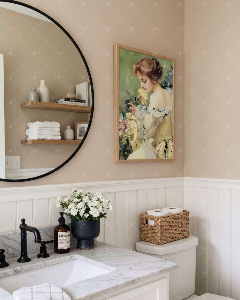 Puede incluir: Una impresi&oacute;n art&iacute;stica rectangular enmarcada que muestra el retrato de una persona con cabello casta&ntilde;o sosteniendo una flor amarilla, exhibida en un ba&ntilde;o con un espejo redondo de marco negro, un tocador de m&aacute;rmol y una cesta tejida.