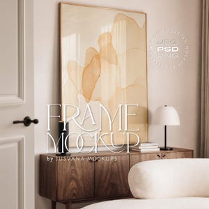 Puede incluir: Una obra de arte enmarcada con formas abstractas de acuarela naranja y beige cuelga sobre un mueble de madera. El mueble tiene una lámpara, libros y un jarrón negro. El texto "FRAME MOCKUP" se muestra en la obra de arte.