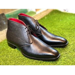 Puede incluir: Un par de botines de cuero negro con cierre de cordones y punta puntiaguda. Los botines tienen una parte superior de cuero texturizado y un forro rojo.