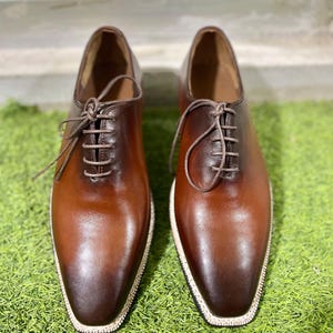 Puede incluir: Un par de zapatos marrones de cuero con cordones y un borde blanco alrededor de la suela.