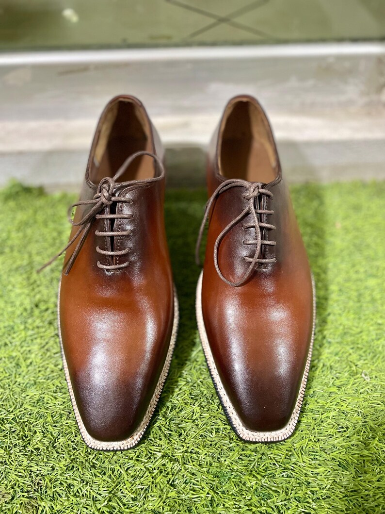 Puede incluir: Un par de zapatos marrones de cuero con cordones y un borde blanco alrededor de la suela.