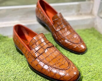 May include: A pair of brown leather loafers with a crocodile pattern. The loafers have a pointed toe and a slip-on design.