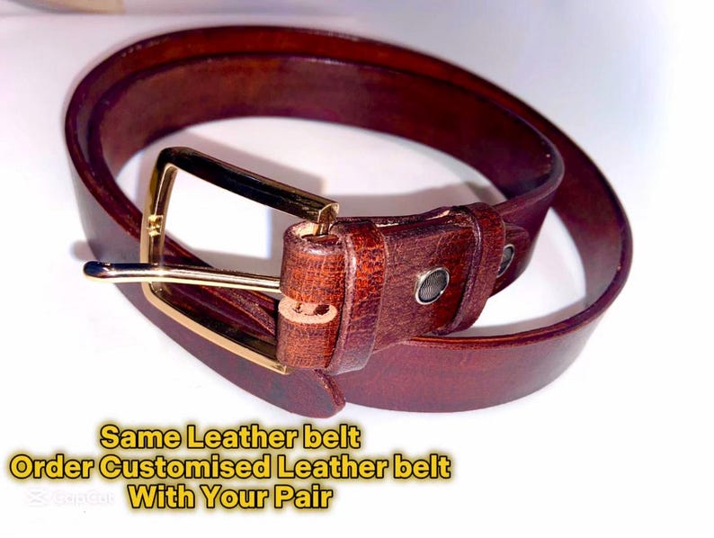 Puede incluir: Un cintur&oacute;n de cuero marr&oacute;n con una hebilla dorada. El cintur&oacute;n est&aacute; doblado por la mitad y la hebilla es visible. El texto "Same Leather belt Order Customised Leather belt With Your Pair" es visible debajo del cintur&oacute;n.