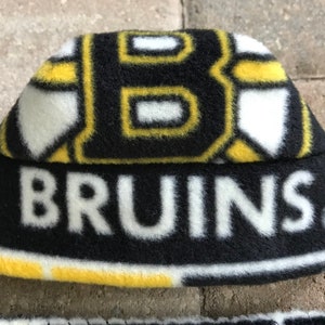 May include: A black, yellow, and white fleece beanie hat. The hat features the word "BRUINS" in white block letters across the front. The top of the hat has a repeating pattern of the letter "B" in black and yellow.
