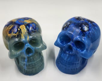 May include: Two blue and gold skull dice with different dice faces embedded in the top of each skull.