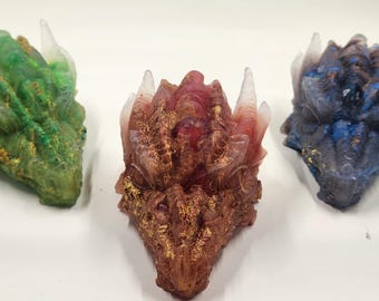 May include: Three dragon head sculptures made of resin with gold accents. The dragon heads are green, red, and blue.