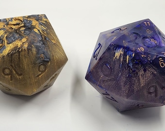 May include: Two large, twenty-sided dice. One is gold and navy blue, the other is purple and blue, both with gold accents. The dice are numbered with gold numerals. The dice have a marbled, swirled appearance.