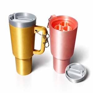 Op de afbeelding: Twee geïsoleerde reisbekers. Eén is goudkleurig met een grijze deksel en handvat, de andere is roze met een ingebouwde houder voor meerdere items. Een losse grijze deksel is ook aanwezig. Beide hebben een vergelijkbare vorm.