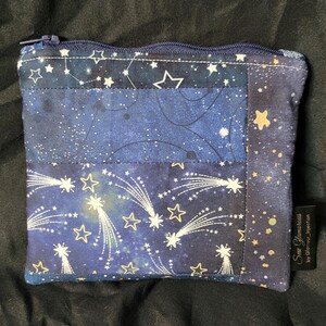 May include: A blue zippered pouch with a patchwork design featuring a starry night sky with shooting stars and gold stars. The pouch has a label that reads "Star Glamorous by Glamour_Injection".