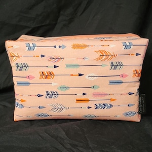 May include: A pink zippered pouch with a repeating pattern of colorful arrows. The pouch has a black tag with the text "Sun & Moon" and "Handmade in Australia".