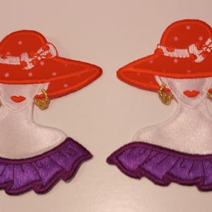 May include: Two embroidered patches featuring a woman in a red hat with white polka dots and a white ribbon. The woman has gold earrings, red lips, and a purple ruffled collar. The patches are ideal for clothing or accessories.