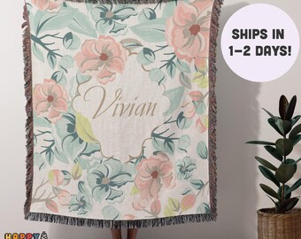 May include: A woven throw blanket with a floral pattern in shades of pink, green, and white. The blanket has a fringe border and features the name "Vivian" in a decorative font.