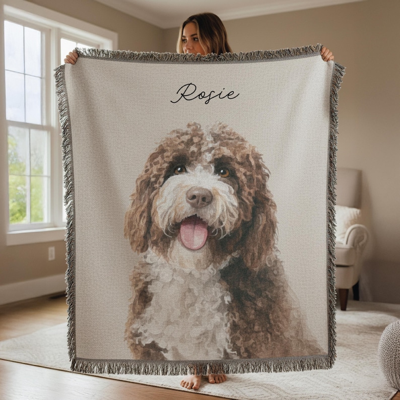 Puede incluir: Una manta tejida beige con un retrato de un perro marr&oacute;n y blanco. El nombre del perro, "Rosie", est&aacute; escrito en cursiva. La manta tiene un borde con flecos. El retrato del perro es el foco principal.