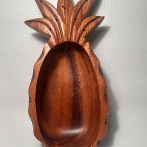 May include: A wooden pineapple-shaped bowl with a carved design. The bowl is made of dark brown wood and has a smooth, polished finish.