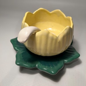 Peut inclure: Un bol en céramique jaune en forme de fleur avec une cuillère blanche, posé sur une soucoupe en céramique verte en forme de feuille.