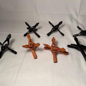 May include: Seven wooden display stands in black and reddish-brown. Each stand has a three-legged design with a central support structure. These stands are designed to hold items, offering a decorative and functional display solution.