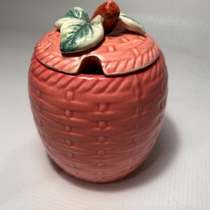 May include: A pink ceramic sugar bowl shaped like an apple with a green leaf and red stem lid.