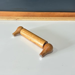 Peut inclure: Un porte-papier toilette en bois avec des extrémités arrondies. Le porte-papier est en bois brun clair et a un design simple.