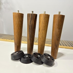 May include: Four wooden furniture legs with a dark brown wood grain finish. Each leg has a metal screw at the top and a black plastic base.