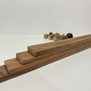 Puede incluir: Cuatro tablas de madera apiladas una encima de la otra, con la tabla más grande en la parte inferior y la más pequeña en la parte superior. Las tablas son de color marrón claro y tienen una superficie lisa.