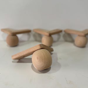 May include: Four unfinished wooden furniture legs. Each leg features a rounded base and a right-angled top piece. The wood has a natural, light brown color. The legs are designed for furniture construction or repair.