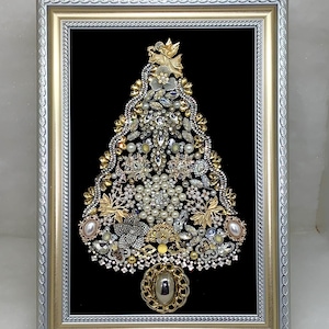 May include: A framed wall art piece featuring a Christmas tree shape constructed from an assortment of vintage jewelry, including gold-tone metal pieces, clear rhinestones, and white pearls, all set against a black background in a silver frame.