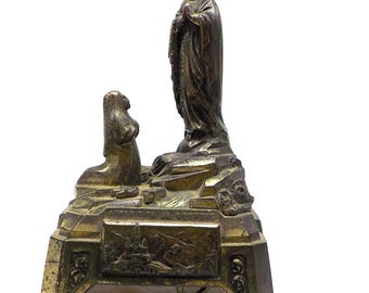 May include: A gold-toned metal figurine depicting the apparition of the Virgin Mary at Lourdes. The figurine features a kneeling figure of a woman in front of a standing figure of the Virgin Mary. The base of the figurine is inscribed with the text "Apparition de Lourdes".