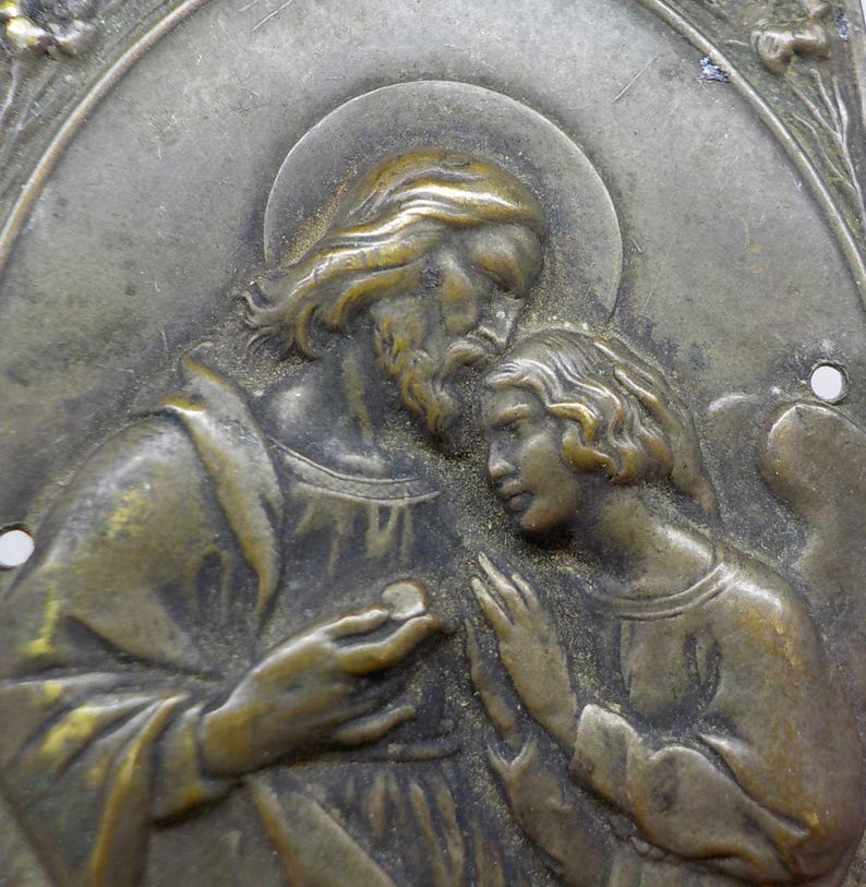 May include: Antique bronze religious plaque depicting a bearded figure with a halo, offering a small disc to a younger figure. The figures are in relief against an oval background, with floral accents and two small holes for hanging.