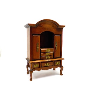 May include: A wooden cabinet with a curved top, two doors, and four drawers. The cabinet has a brown finish and brass hardware.