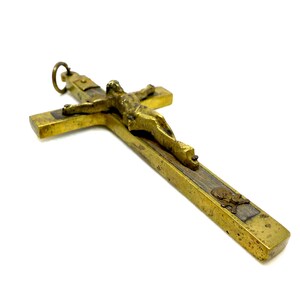 Könnte beinhalten: Ein goldfarbenes Messingkreuz mit einer Holzeinlage und einem kleinen Totenkopf- und Knochenmotiv. Das Kruzifix zeigt eine detaillierte Figur von Jesus Christus.